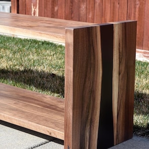 May include: A wooden bench with a black epoxy inlay in the side. The bench has two shelves and is made of walnut wood.