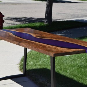 May include: A wooden table with a live edge top and a purple resin river running through the center. The table has black metal legs.