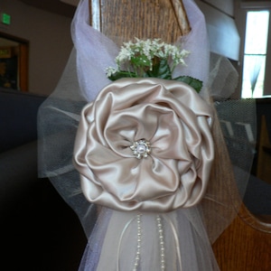 May include: A white satin flower with a pearl embellishment, attached to a sheer white tulle fabric with a beaded trim.