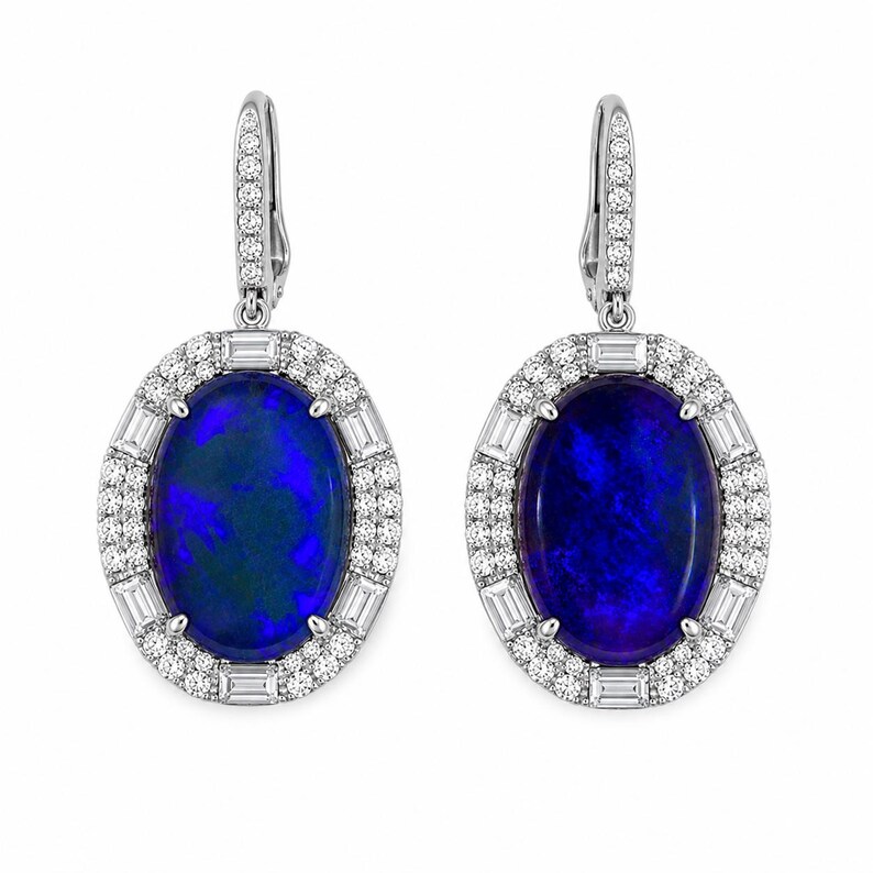 May include: A pair of oval-shaped earrings featuring a deep blue opal stone surrounded by a halo of small round diamonds and baguette-cut diamonds. The earrings have a lever back closure and are set in white metal.