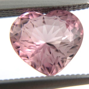 May include: A heart-shaped, faceted gemstone with a pink hue and a starburst pattern.