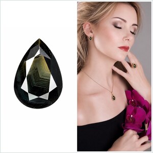 Puede incluir: Una piedra preciosa en forma de pera, con una combinación de colores verde oscuro y negro. La imagen también muestra a una mujer que lleva un conjunto de joyas a juego, que incluye pendientes, un collar y un anillo, todos con la misma piedra preciosa.