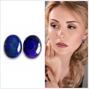 May include: Two oval-shaped opals with a dark blue and green iridescence. The opals are displayed on a white background. The image also shows a woman wearing matching jewelry: earrings and a ring with similar blue gemstones.