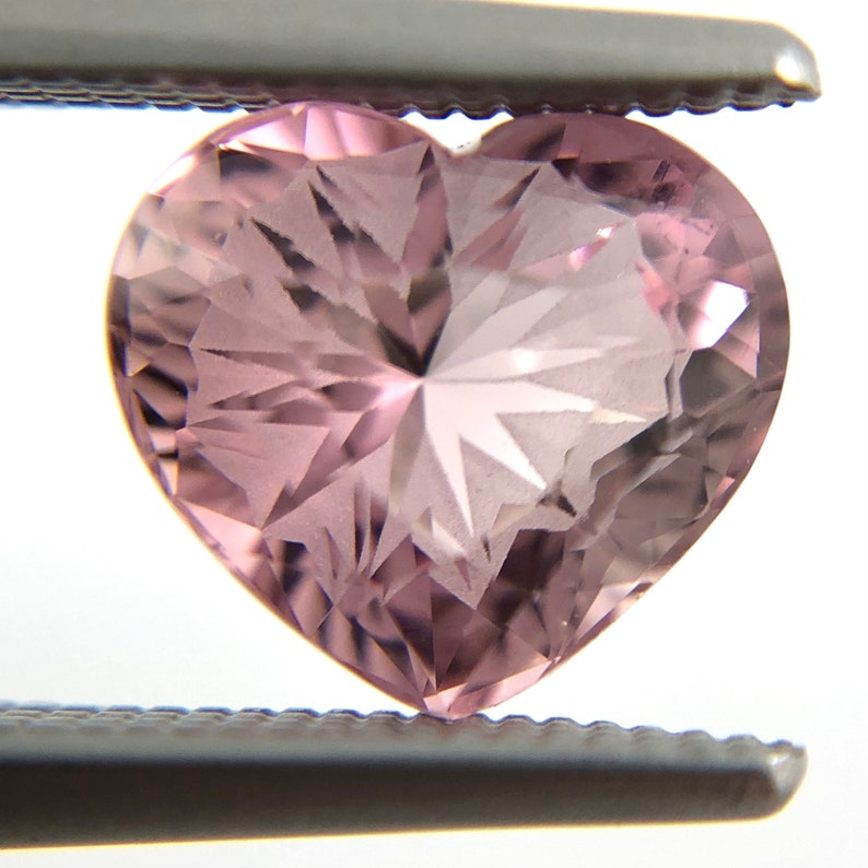 May include: A heart-shaped, faceted, pink gemstone with a starburst pattern.