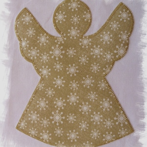 May include: A gold-colored angel-shaped applique with white snowflake patterns. The applique has a stitched border and is set against a white background. This decorative item is suitable for holiday crafts and decorations.