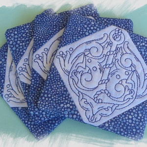 May include: Set of four square coasters. Each coaster features a white, embroidered anchor design on a blue and white polka dot background. The anchor design is surrounded by decorative swirls and rope details. The coasters are made of fabric.