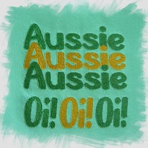 以下が含まれることがあります： 緑と金の刺繍パッチ。"Aussie"という単語が3回繰り返され、感嘆符の"O!"が3回繰り返されています。