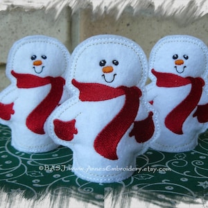 May include: Three white felt snowman ornaments with red felt scarves. The snowmen have black embroidered eyes and mouths and orange felt noses.