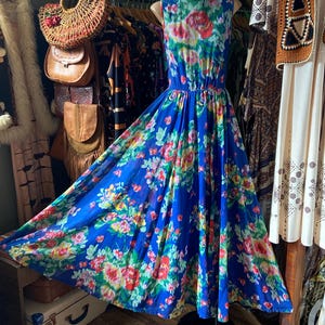 Può includere: Un abito blu senza maniche, lungo fino al pavimento, con un motivo floreale di fiori rossi, rosa, gialli e verdi. L'abito ha un corpetto aderente e una gonna fluida. L'abito è esposto su un manichino.