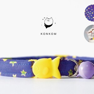 May include: A purple cat collar with a yellow fish-shaped buckle, a purple bell, and a blue and yellow star pattern. The collar is on a white background. The text "KONKOM" is visible in the image.