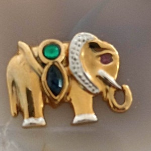 May include: A gold elephant charm with green, blue, and red gemstones. The elephant is standing on its four legs and has a trunk raised in the air.