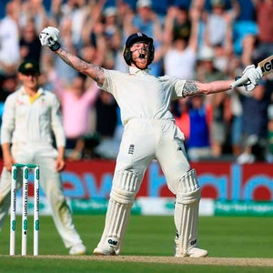 Puede incluir: Un jugador de cricket con un uniforme blanco levanta su bate en celebración después de golpear un seis. Lleva un casco y protectores. El jugador está de pie en un campo verde con una línea blanca y una multitud de personas en el fondo.