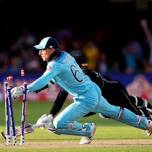 Puede incluir: Un jugador de cricket con un uniforme azul se lanza para intentar romper los wickets, mientras que otro jugador con un uniforme negro observa.