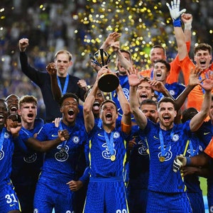 Puede incluir: Un grupo de jugadores de fútbol con uniformes azules y naranjas celebran con un trofeo. Están sosteniendo el trofeo y sonriendo. Hay confeti cayendo a su alrededor.