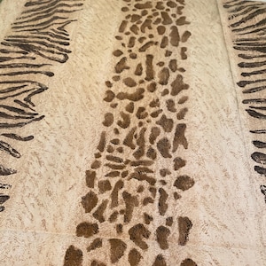 May include: A beige textile with a repeating pattern of brown zebra stripes and leopard spots. The design features a central column of leopard spots flanked by zebra stripes on either side, creating a textured, animal print aesthetic.
