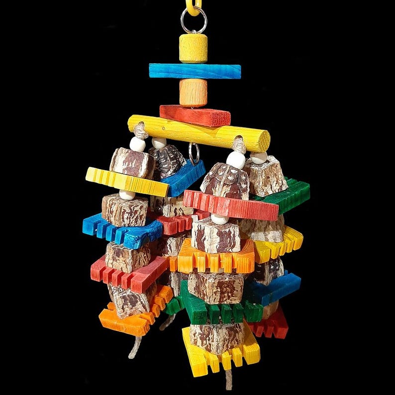 Layers of soft mahogany pod chunks, brightly colored notched pine busy beaver slices and small wood snap beads flowing under a wood dowel base on jute cord. Hangs on a short length of nickel plated chain with more wood pieces. Designed for intermediate to medium sized birds who like softer textures (cockatiels, small conures, quakers, caiques, greys, etc). Measures approx 5" by 10" including link.