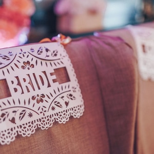 Banderines personalizados de papel picado con motivos florales para las sillas de los novios.