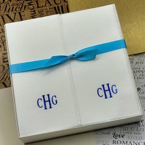 May include: A white gift box with a blue ribbon tied around it. The box is monogrammed with the initials "CHG".