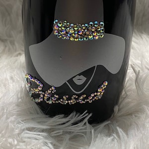 May include: Black ceramic mug with a white silhouette of a woman wearing a hat with rhinestones. The word "Blessed" is spelled out in rhinestones below the woman.