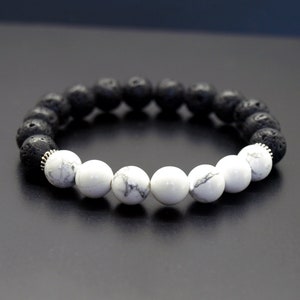 以下が含まれることがあります： 黒溶岩と白ハウライトのビーズを交互に配置したブレスレット。 ブレスレットは、さまざまな質感と色の組み合わせのシンプルなデザインです。 テキスト「ShortandBaldJewelry」が右上に表示されています。