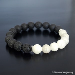 May include: A black lava rock and white moonstone beaded bracelet with silver spacers. The bracelet is made of natural stones and is designed to be worn on the wrist.