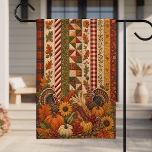 May include: A rectangular garden flag featuring a vertical patchwork design with autumn-themed stripes of plaid, leaves, acorns, and gingham. The bottom section displays two turkeys, orange and white pumpkins, sunflowers, and corn stalks in fall colors.