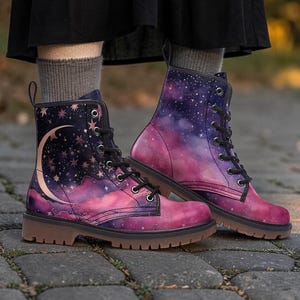 May include: Combat boots with a celestial design. The boots feature a galaxy print in shades of purple, pink, and blue, with a crescent moon and stars on the outer side. They have black laces and a brown sole.