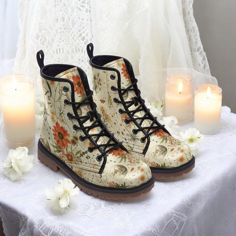 May include: A pair of cream-colored leather boots with black laces and a floral print featuring sunflowers, moons, and stars. The boots have a brown rubber sole.