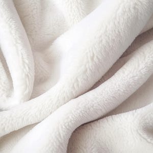 May include: Close-up of a soft, white, plush blanket. The fabric is folded and draped, creating shadows and highlights that emphasize its texture. The blanket appears fluffy and inviting, suggesting warmth and comfort.