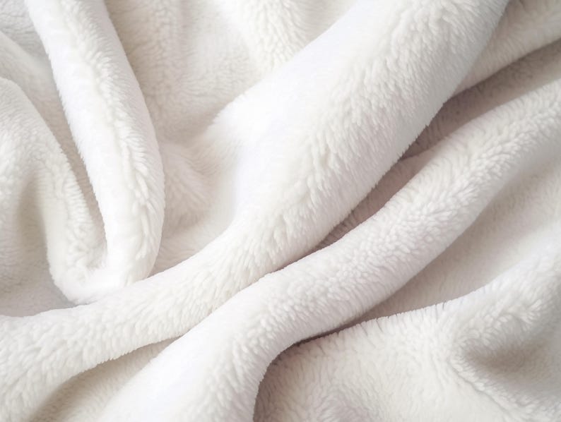 May include: Close-up of a soft, white, plush blanket. The fabric is folded and draped, creating shadows and highlights that emphasize its texture. The blanket appears fluffy and inviting, suggesting warmth and comfort.