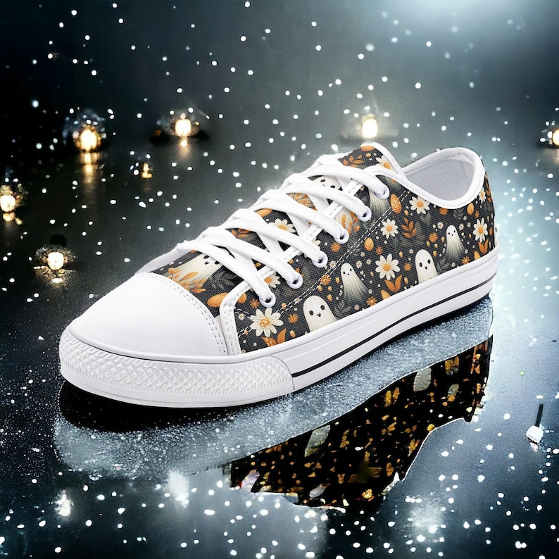 May include: White canvas low-top sneakers with a black and white ghost and floral print. The shoes have white laces and a black rubber sole.