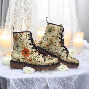May include: A pair of beige ankle boots with brown laces and a floral print featuring constellations and moons. The boots have a brown rubber sole.