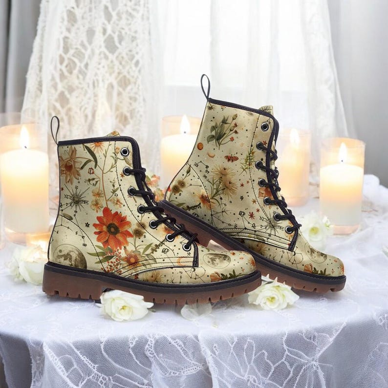 May include: A pair of beige ankle boots with brown laces and a floral print featuring constellations and moons. The boots have a brown rubber sole.