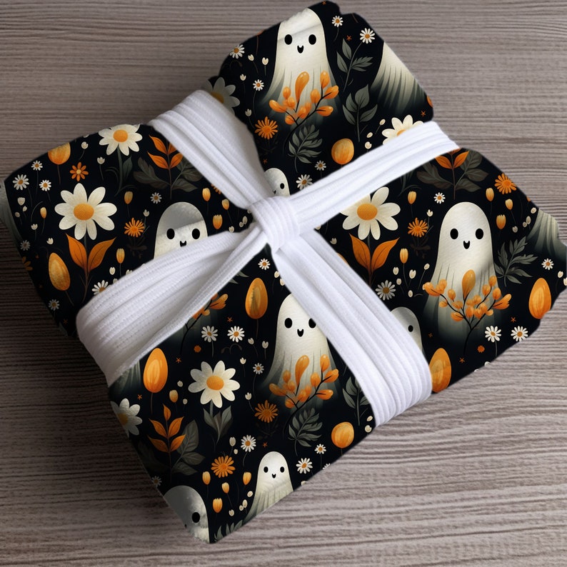 May include: A white fabric gift wrap with a black and white pattern of ghosts and flowers. The fabric is tied with a white ribbon.