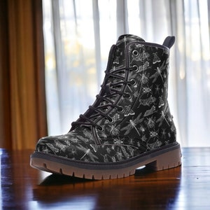 Może przedstawiać: Czarne skórzane buty z wzorem białych ważek i owadów. Buty mają sznurowanie i grubą gumową podeszwę.