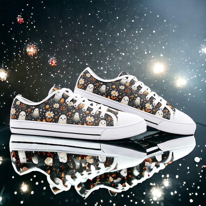 May include: A pair of black and white canvas shoes with a ghost and floral pattern. The shoes have white laces and a white sole.