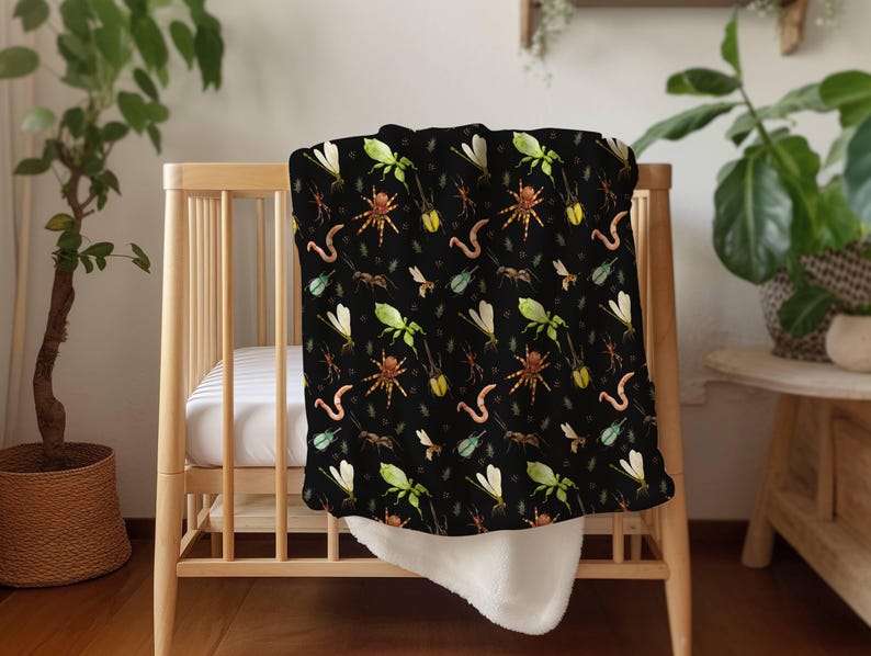 May include: A black baby blanket featuring a repeating pattern of colorful insects, including spiders, dragonflies, and worms. The blanket is draped over a wooden crib, with a white, fluffy underside visible.