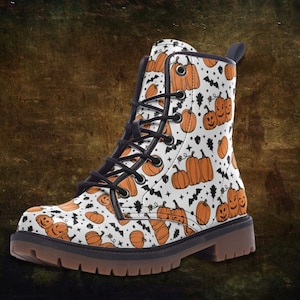 May include: White leather boots with a black lace-up closure. The boots are covered in a pattern of orange pumpkins with black faces.