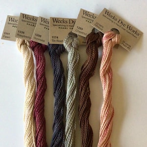 May include: A collection of six skeins of Weeks Dye Works pearl cotton thread in various colors. The colors include fawn, raspberry, gunmetal, tin roof, chestnut, and hibiscus. Each skein is labeled with its color name and number.