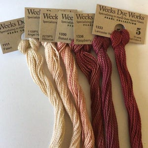 May include: A collection of six skeins of Weeks Dye Works pearl cotton thread in various colors. The colors range from light beige to deep burgundy. Each skein is labeled with a color name and number. The labels are brown with white text.