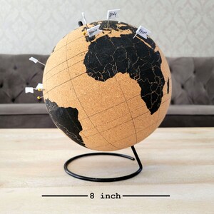 May include: Cork globe with a black map and a metal stand. The globe is 8 inches in diameter and has push pins with flags that say "Italy", "Spain", and "Egypt".