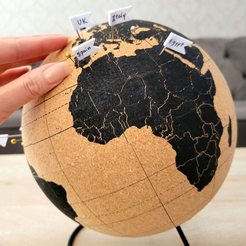May include: A cork globe with a black map of the world. Pins are placed on the globe with labels for UK, Italy, Spain, and Egypt.