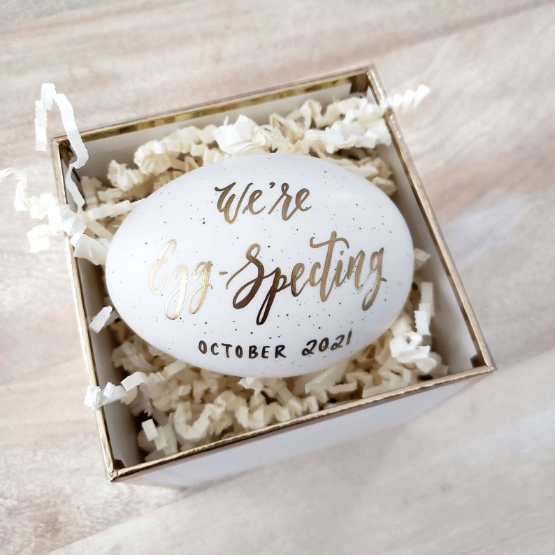 egg with "we're eggspecting" written in elegant gold script