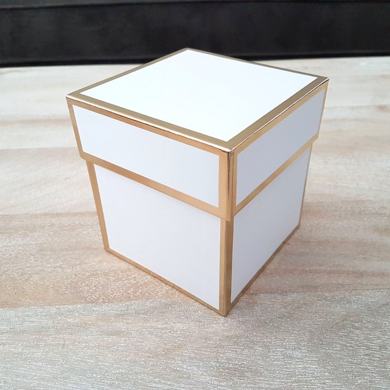 Op de afbeelding: Een witte cadeaudoos met een gouden rand. De doos is vierkant en heeft een deksel.