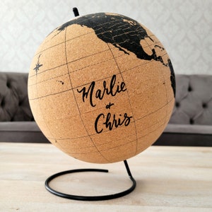 May include: Cork globe with a black metal stand. The globe has a world map printed on it and the text "Marlie & Chris" is written on the front.