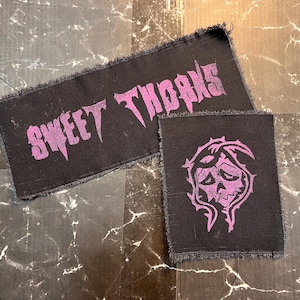 May include: Two black fabric patches with pink lettering. One patch says "Sweet Thorns" and the other has a pink skull with thorns.