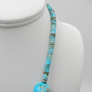 Pu&ograve; includere: Una collana turchese e argento con un grande ciondolo turchese. La collana &egrave; composta da piccole perle rotonde turchesi e da distanziatori argentati.
