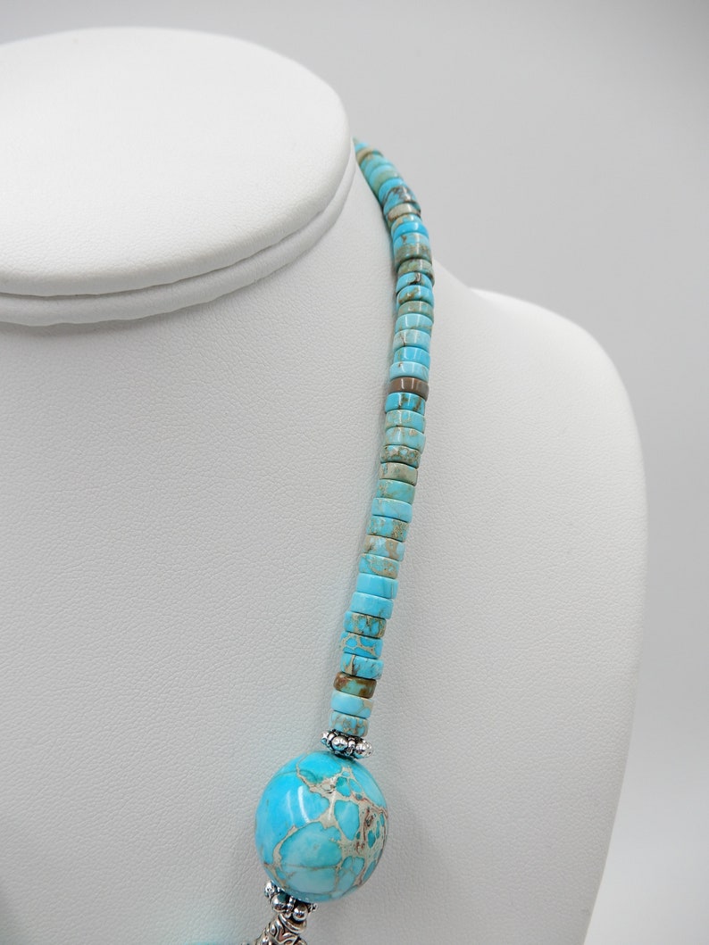 Pu&ograve; includere: Una collana turchese e argento con un grande ciondolo turchese. La collana &egrave; composta da piccole perle rotonde turchesi e da distanziatori argentati.