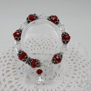 May include: A red carnelian gemstone bracelet with silver accents and clear crystal beads. The bracelet has a dangling red carnelian gemstone charm.