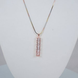 May include: A silver, gold, and rose gold chain necklace with a pendant featuring a vertical bar of clear cubic zirconia stones.